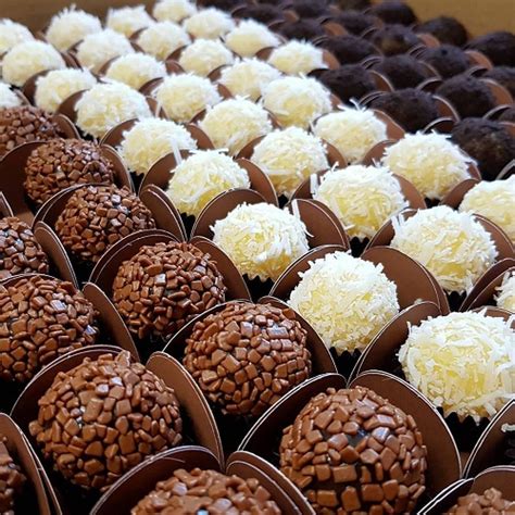 Vários brigadeiros gourmet com cobertura de granulado escuro, branco e ao leite, dispostos de forma organizada sobre uma bandeja, prontos para serem servidos.